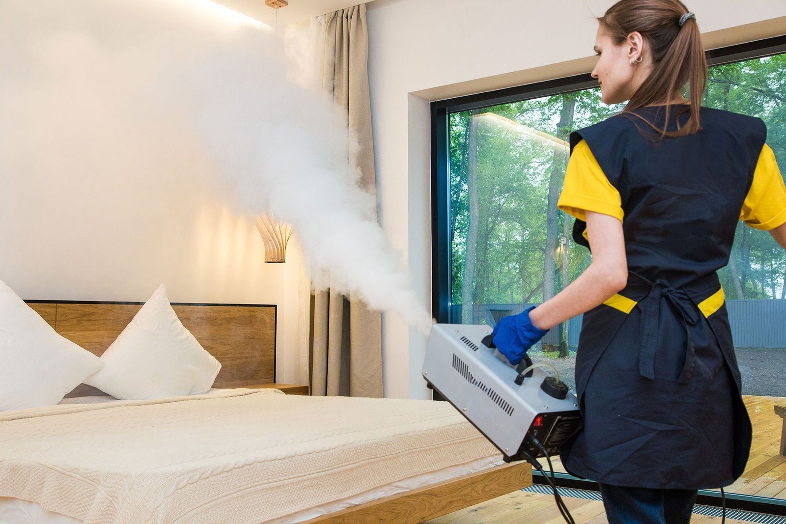Eine Mitarbeiterin vernebelt ein Mittel mit einem Kaltvernebelungsgerät in einem Hotelzimmer